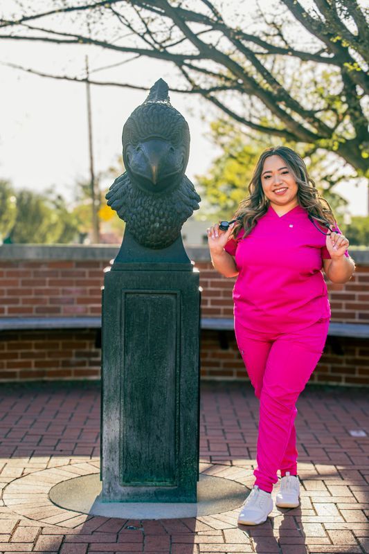 Person in bright pink outfit poses playfully near decorative pillar on brick patio.