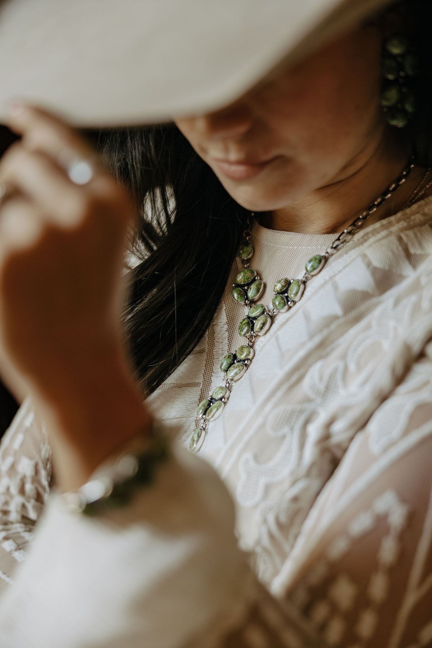Close-up detail of a white lace dress paired with vintage-style green jewelry.