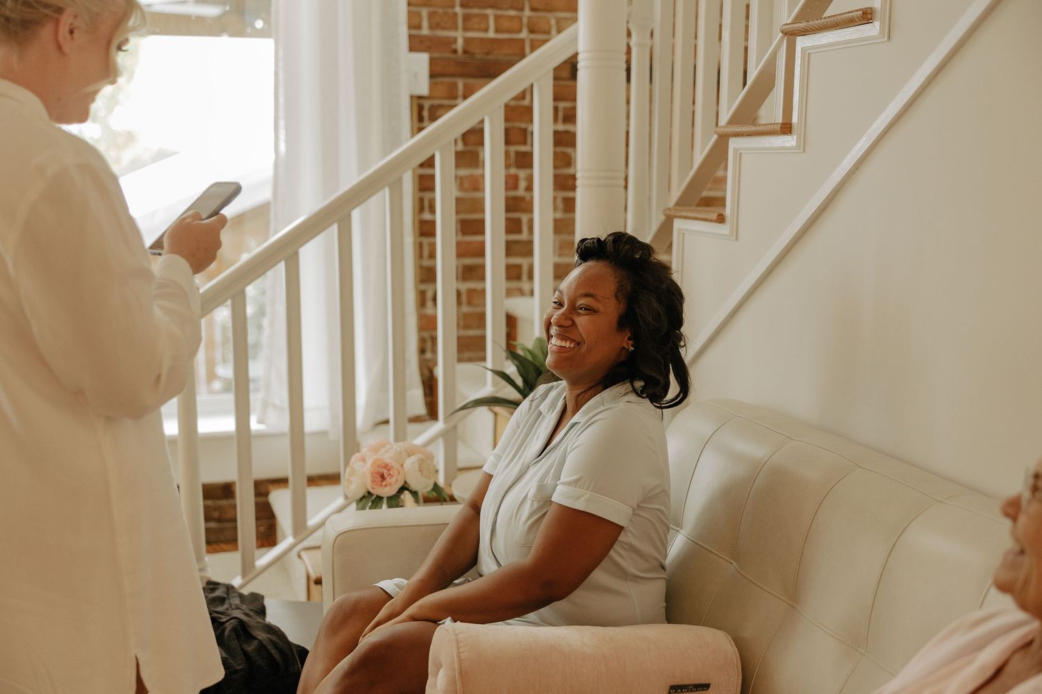 Bridesmaids in white robes sit together on stairs during wedding day preparations.