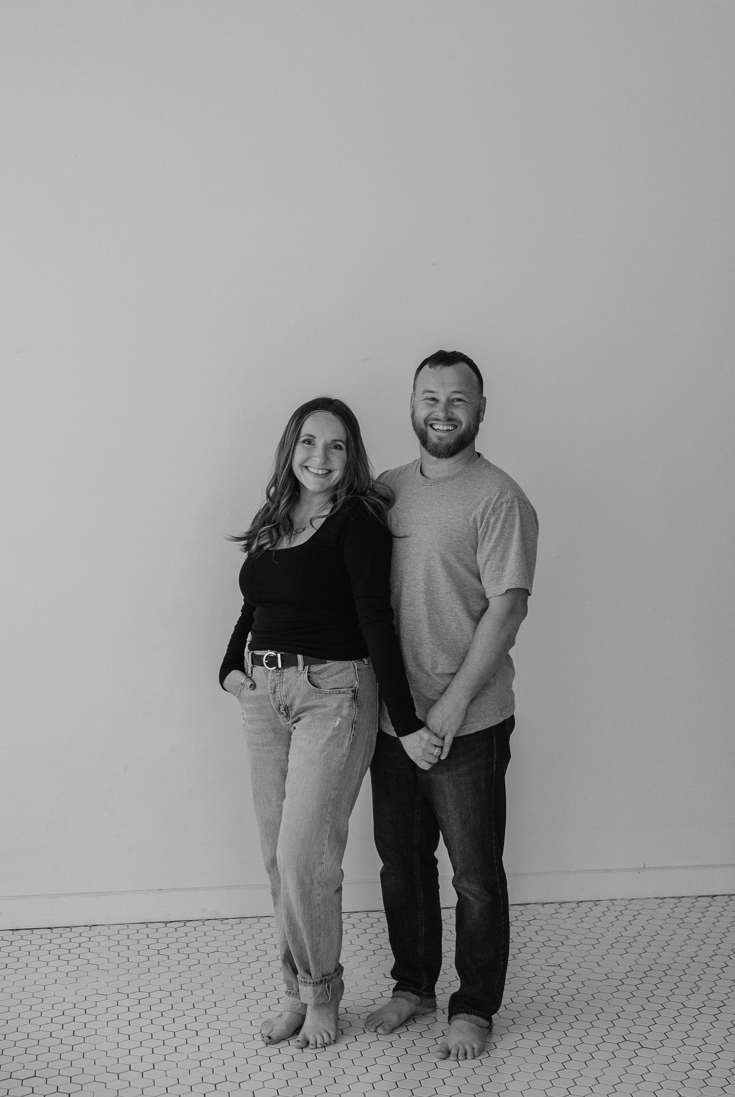 Casual couple portrait in black and white against plain wall showing natural connection.