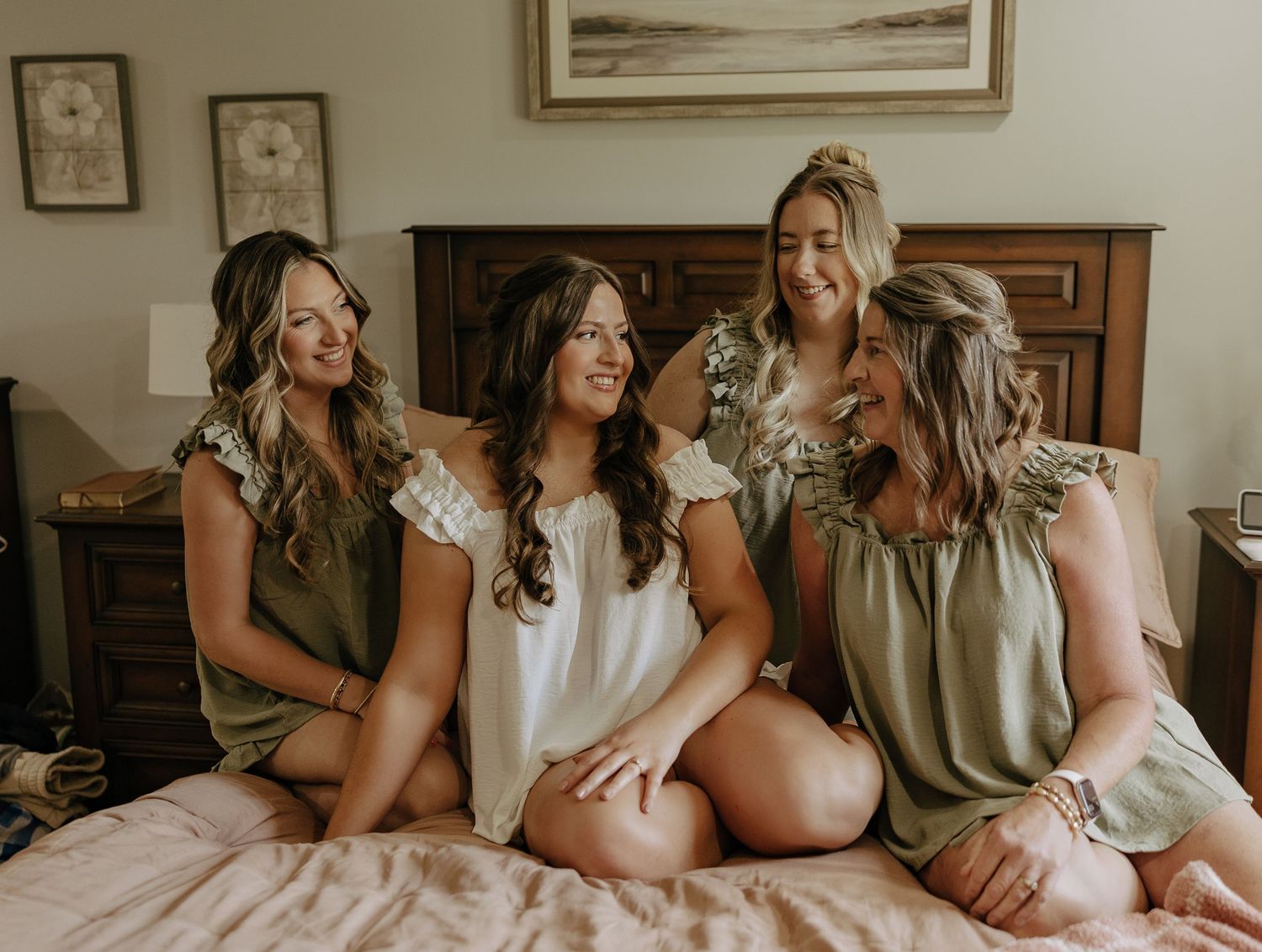 A group of bridesmaids wearing matching robes sit together on a bed during wedding preparations.