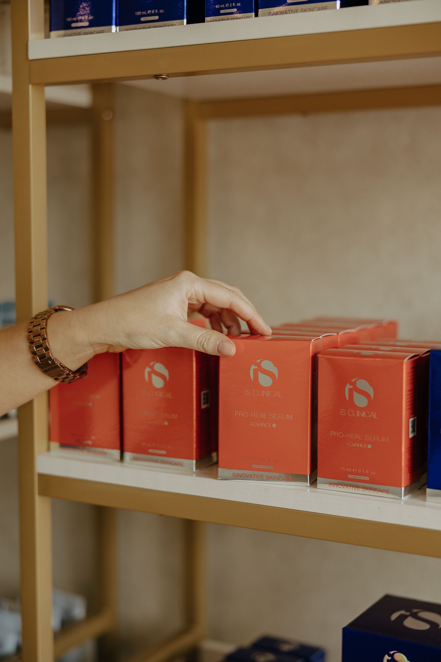 Hand arranging coral colored product boxes on wooden retail shelving.