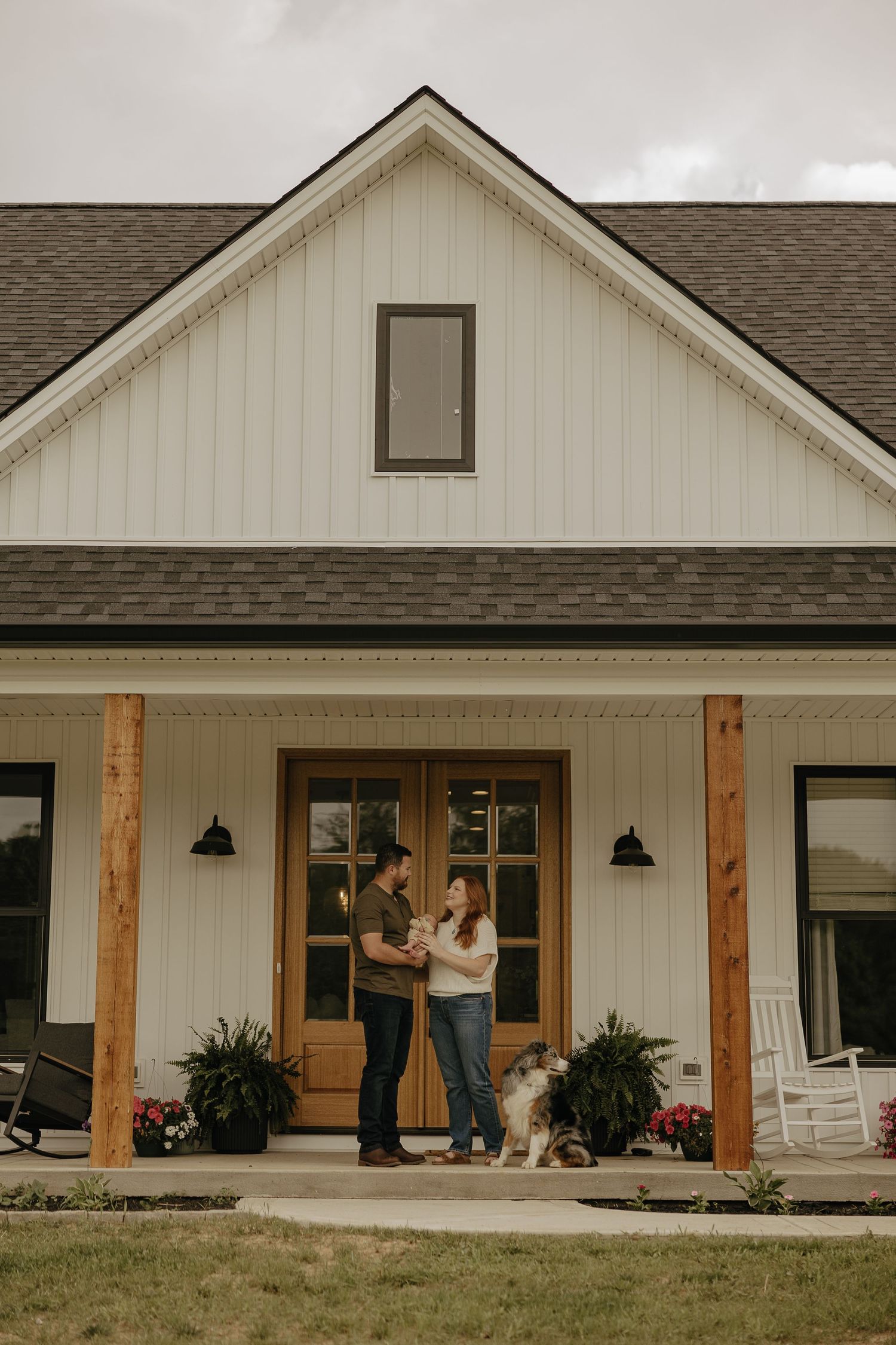 A modern farmhouse with white siding and wooden posts features a spacious front porch.