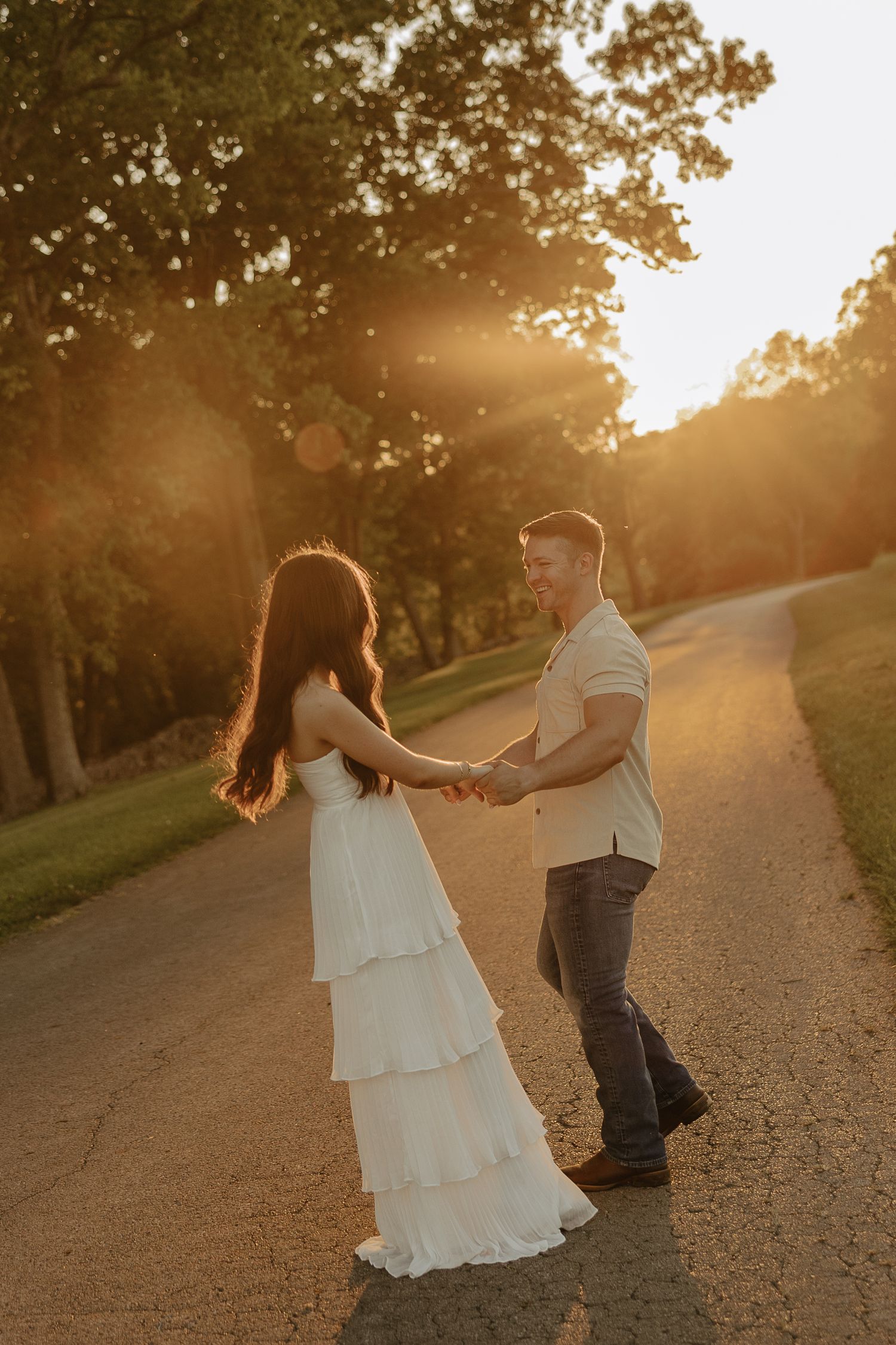 A couple spins and dances together on a golden-lit path during sunset.