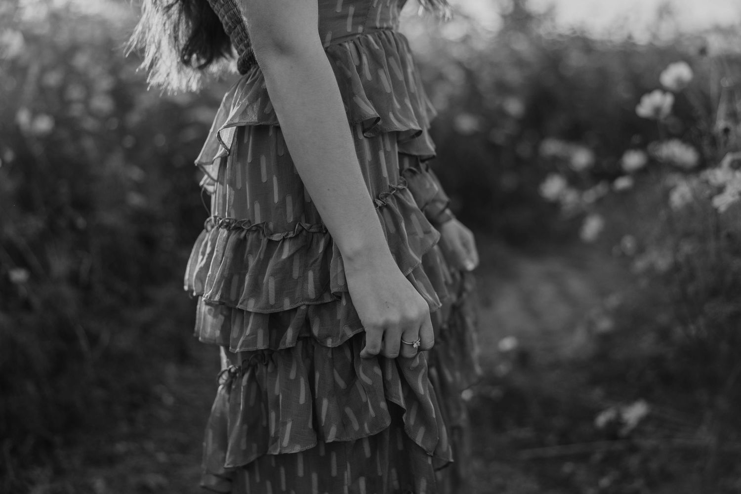 A black and white detail shot of a ruffled dress in a flower field.