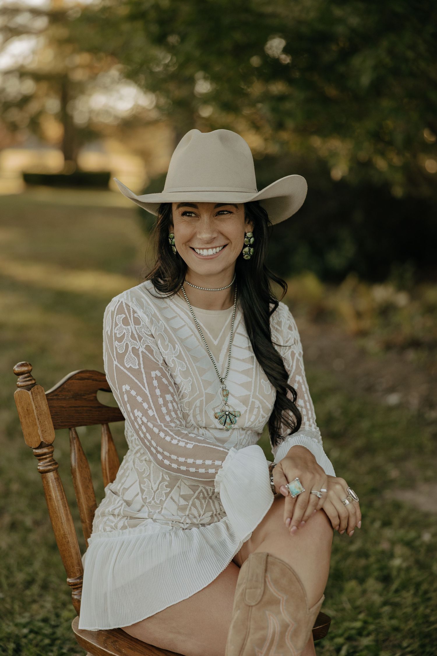 A white lace dress and cowboy hat ensemble photographed outdoors with a wooden chair.