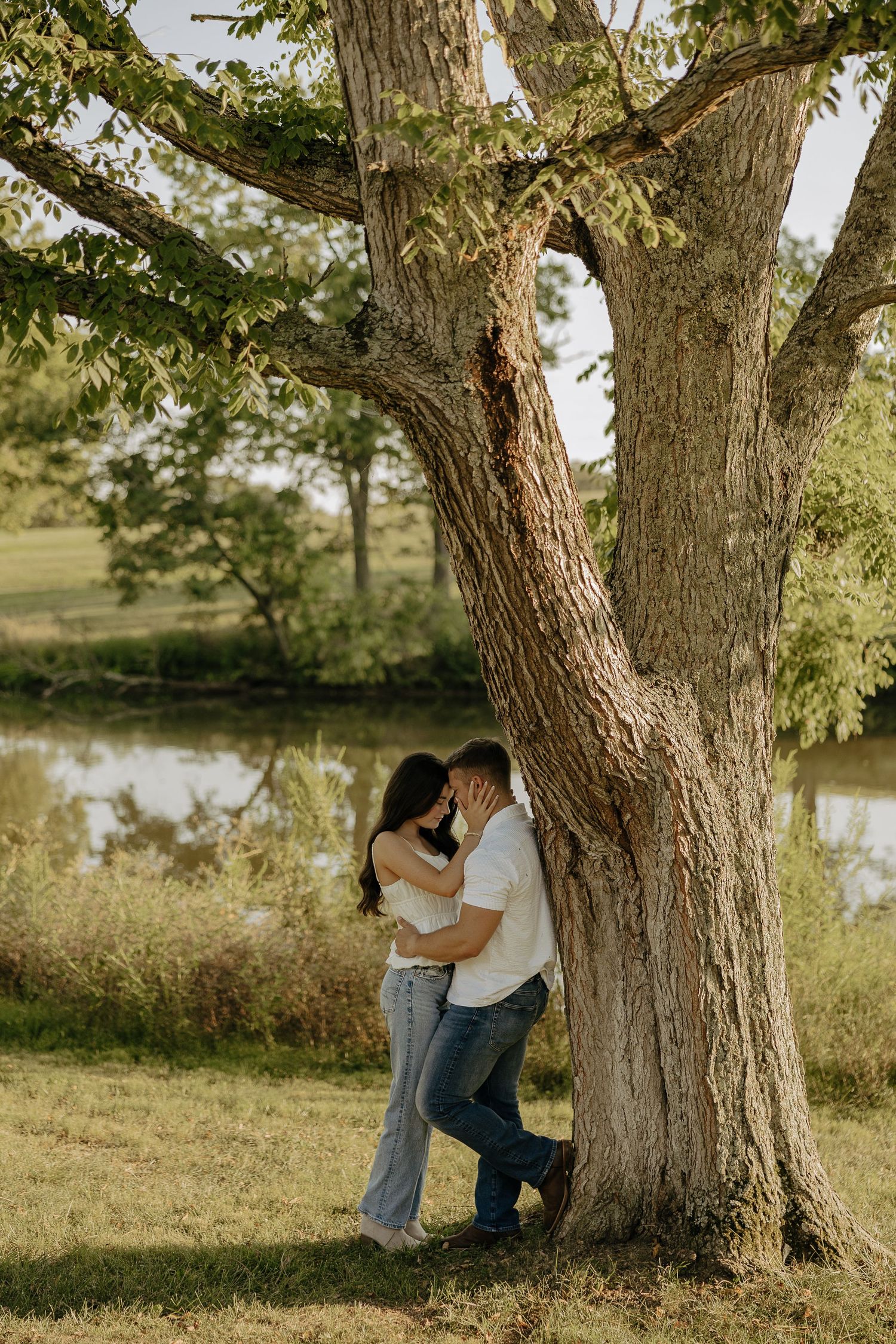 Romantic photoshoot under large tree branches by peaceful pond.