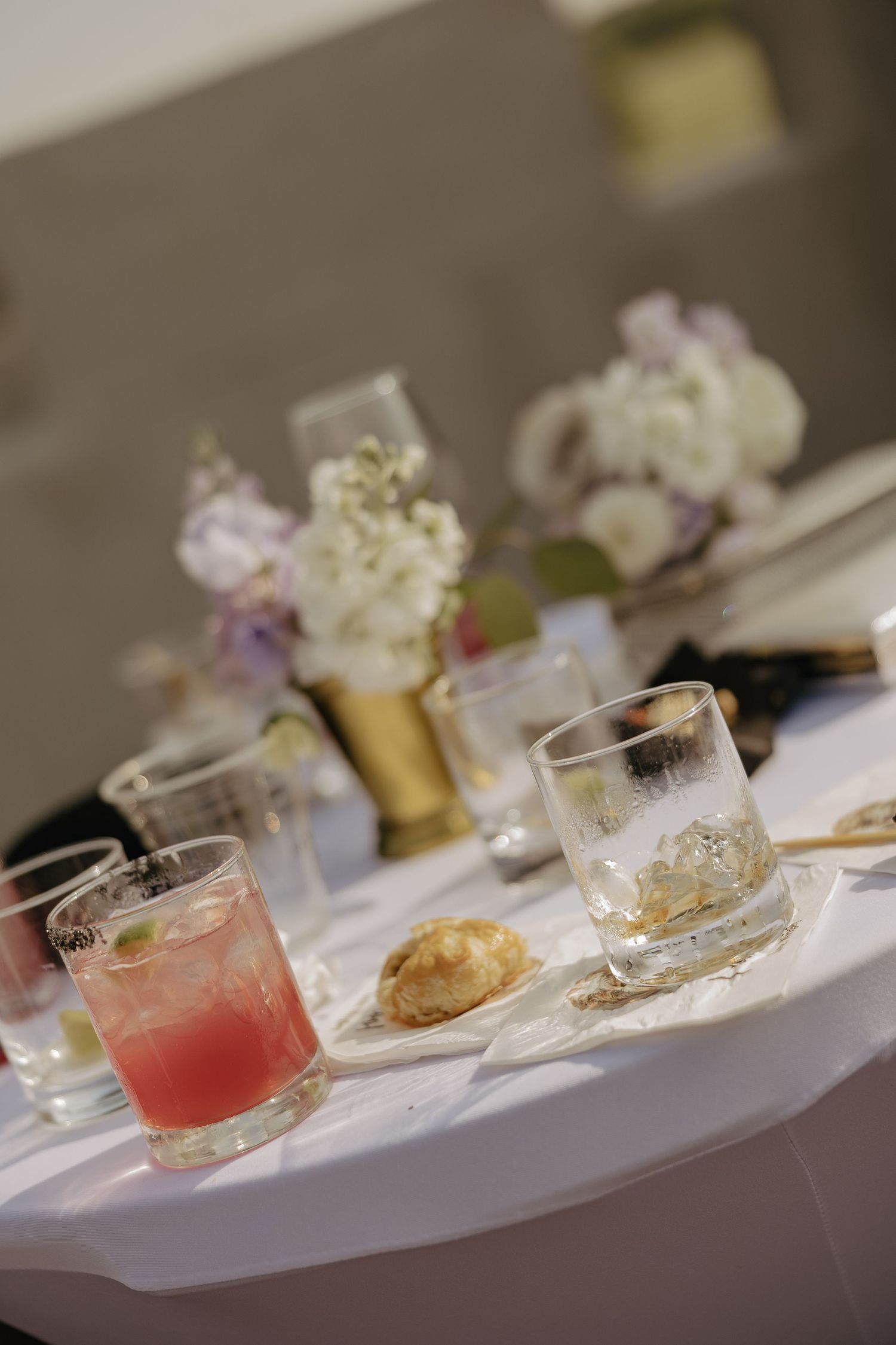 Pink cocktails and floral centerpieces on white tablecloth at wedding reception.