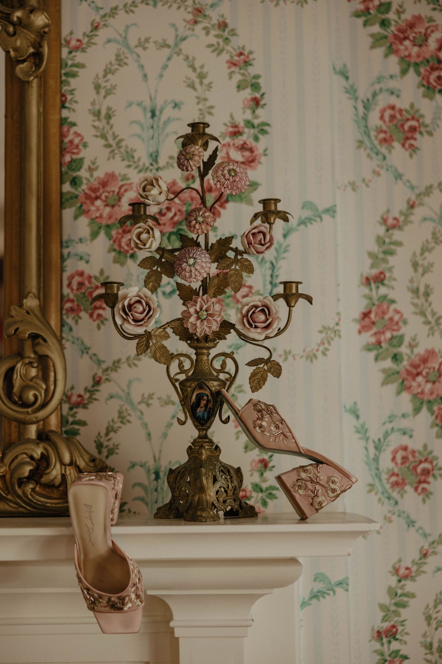 Decorative wall with floral wallpaper featuring antique brass candelabra and ornate gold frame.