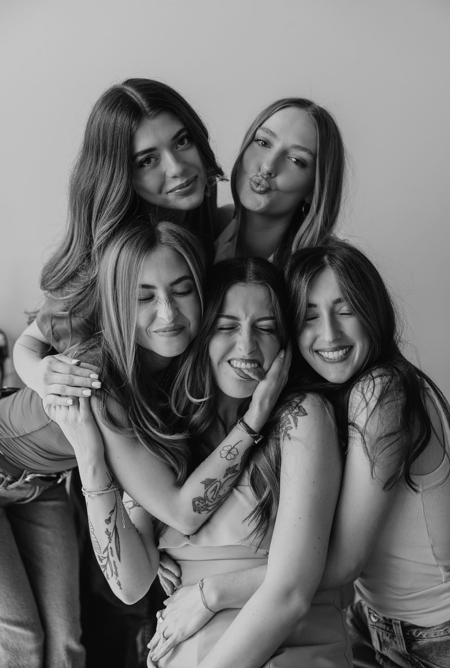 Black and white photo of five young women laughing and embracing in a playful group pose.