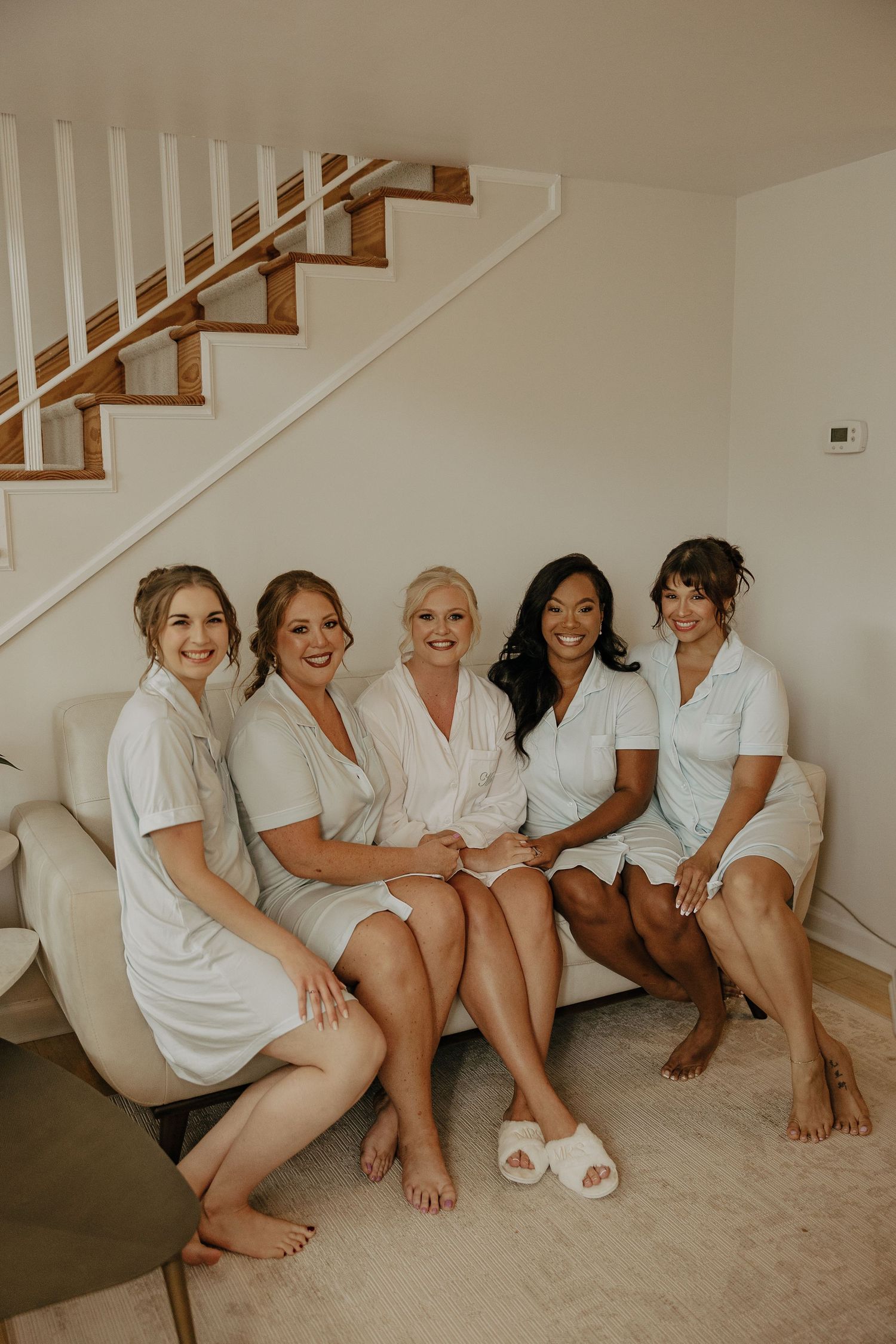 A group wearing matching white robes sits together on a carpeted floor by stairs.