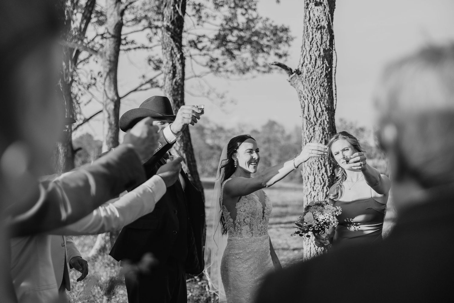 Wedding guests raise their glasses in a celebratory toast during an outdoor ceremony.