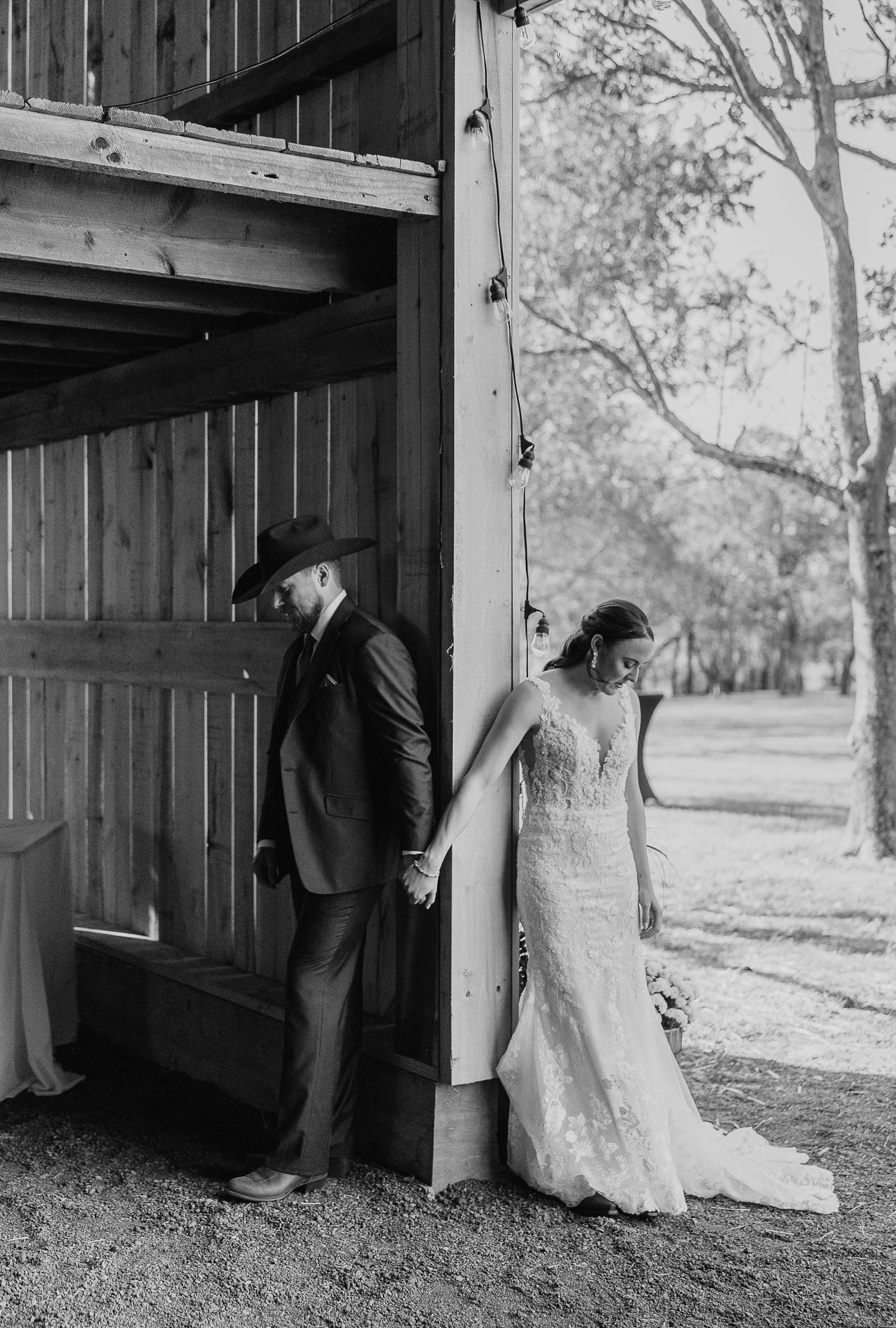 Black and white photo of a couple sharing a private moment against wooden barn walls.
