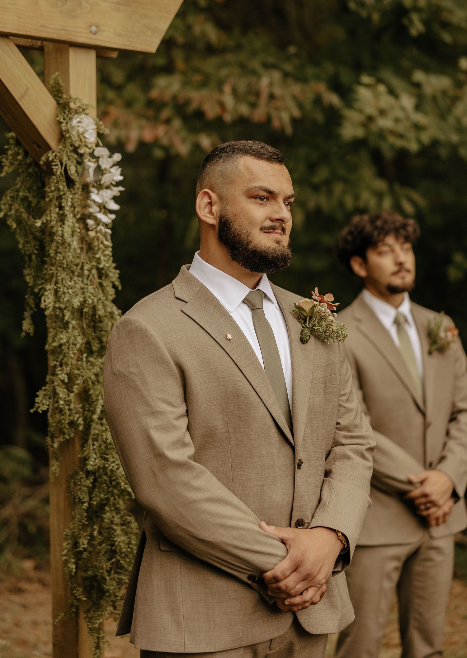 Groomsmen in tan suits standing at attention during outdoor wedding ceremony.