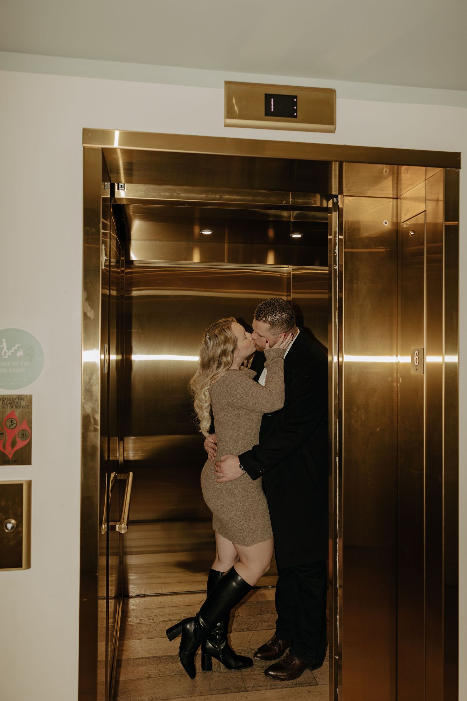 Romantic couple poses near elevator doors in a modern building interior.