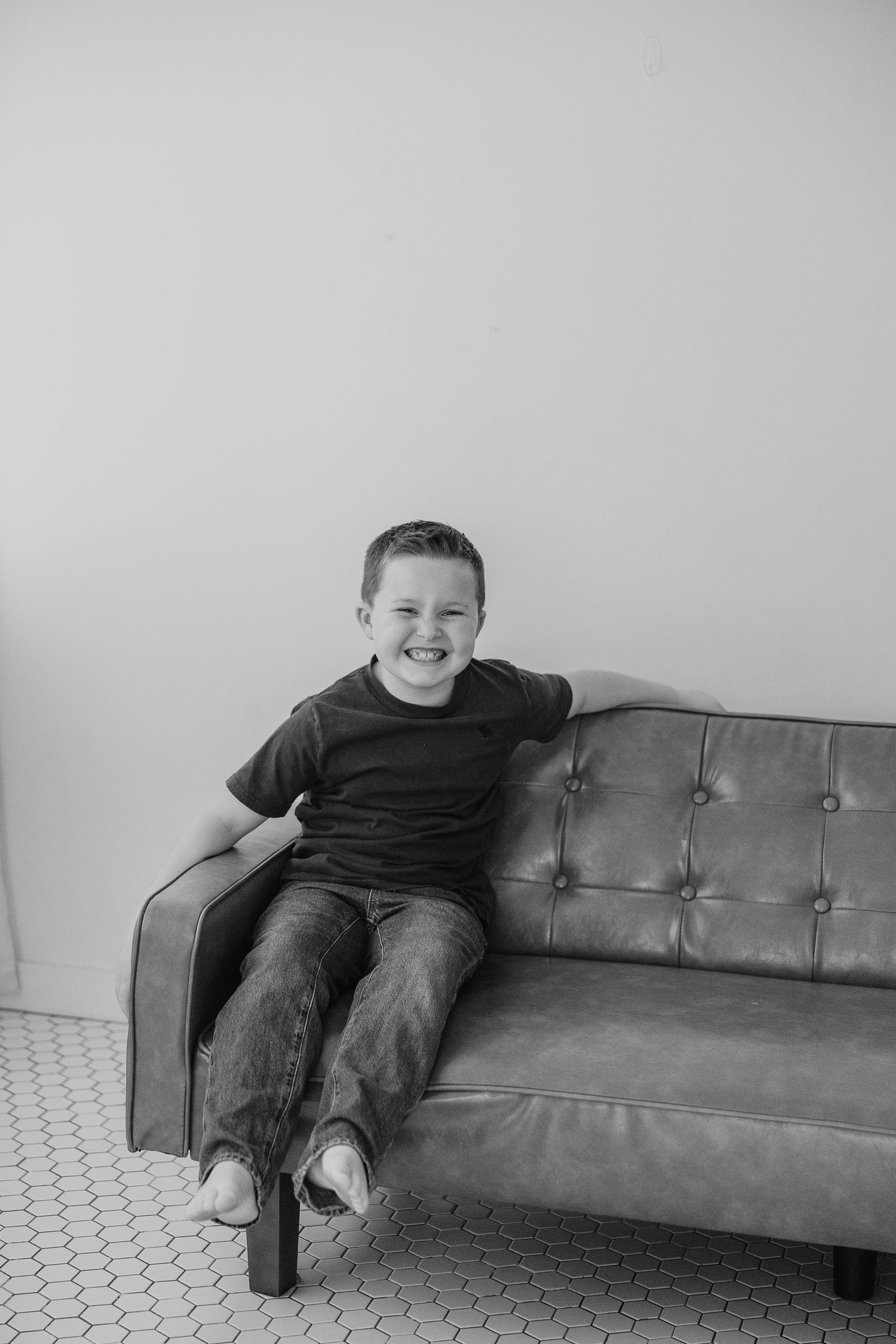 A series of three black and white photos showing a child lounging playfully on a leather tufted sofa.
