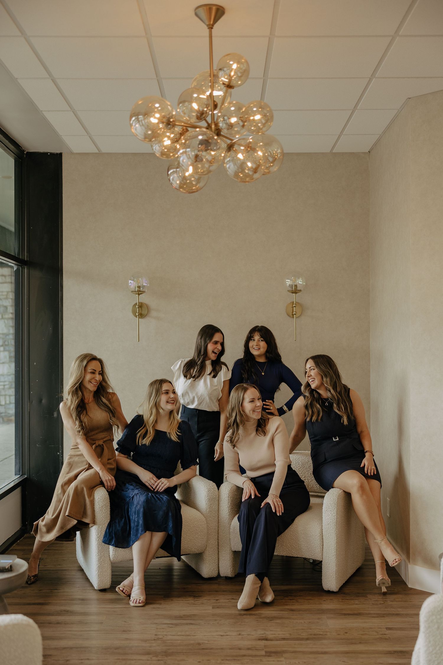 Stylish group portrait of team arranged on cream colored seating with modern chandelier above.