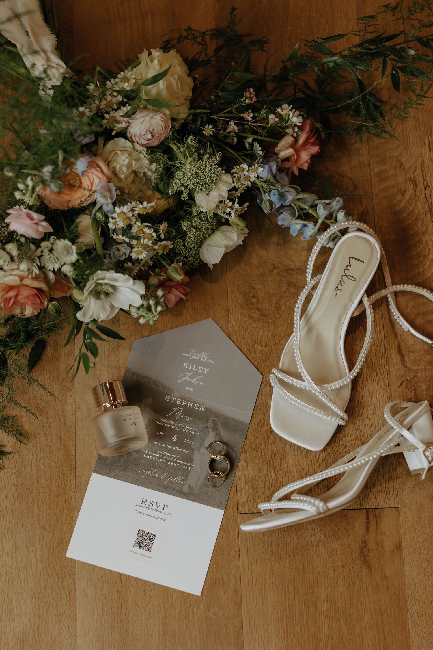 Wedding invitations and floral arrangements displayed on a rustic wooden surface with delicate pink and white flowers.