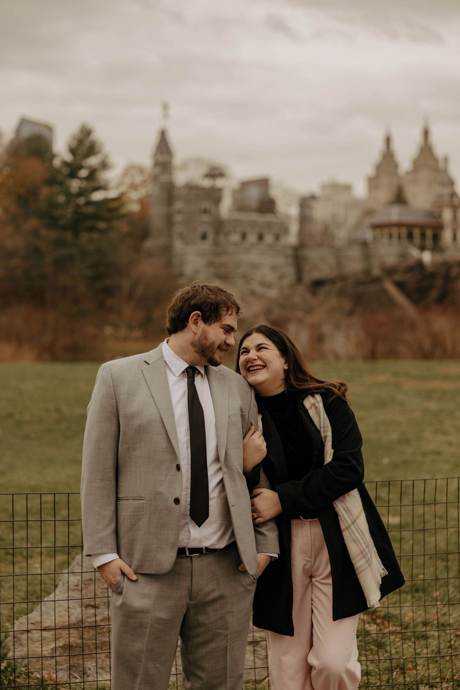 A couple shares a romantic moment together against an autumn backdrop with historic buildings in the distance.