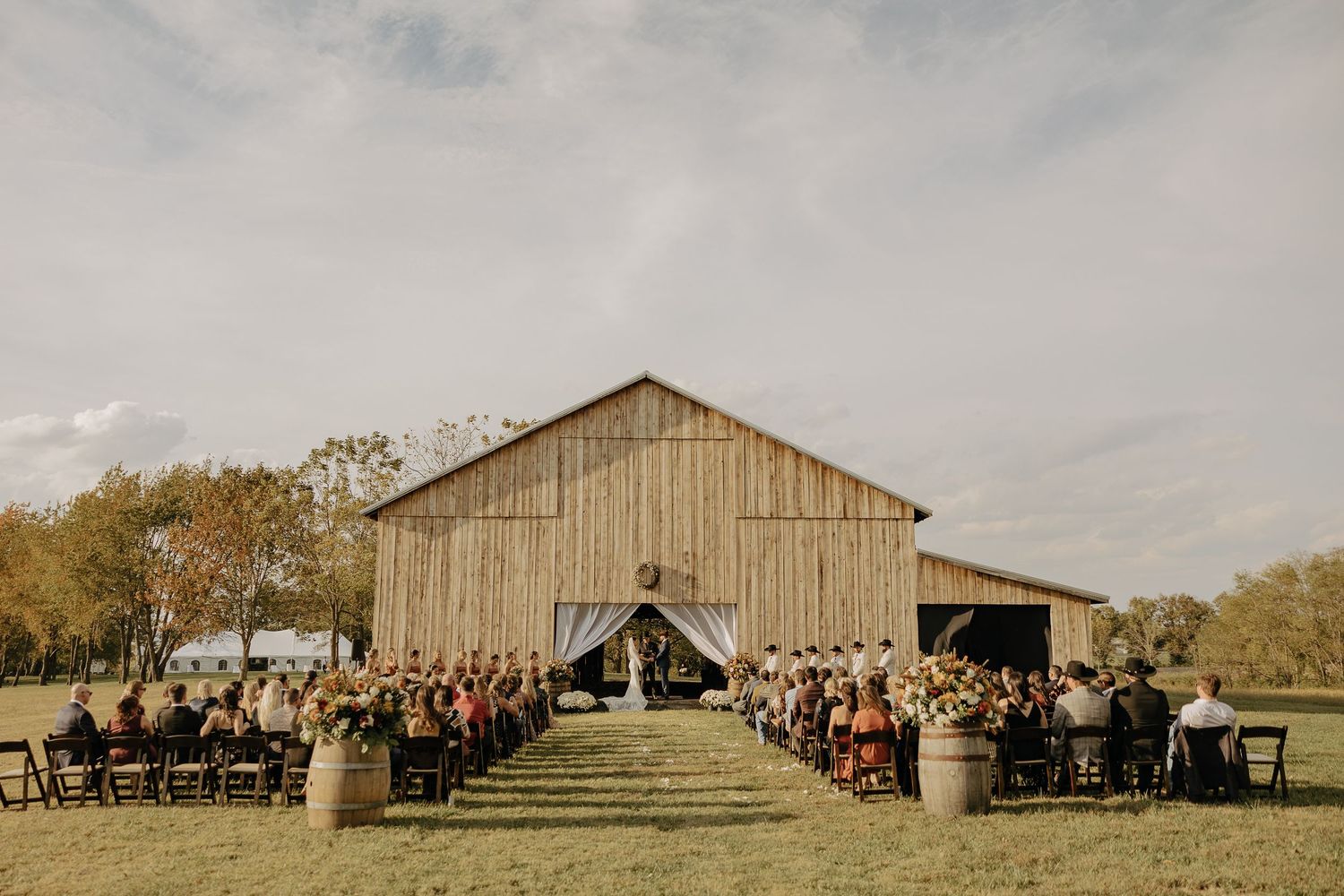 Panoramic view of rustic barn wedding venue with guests gathered outside.
