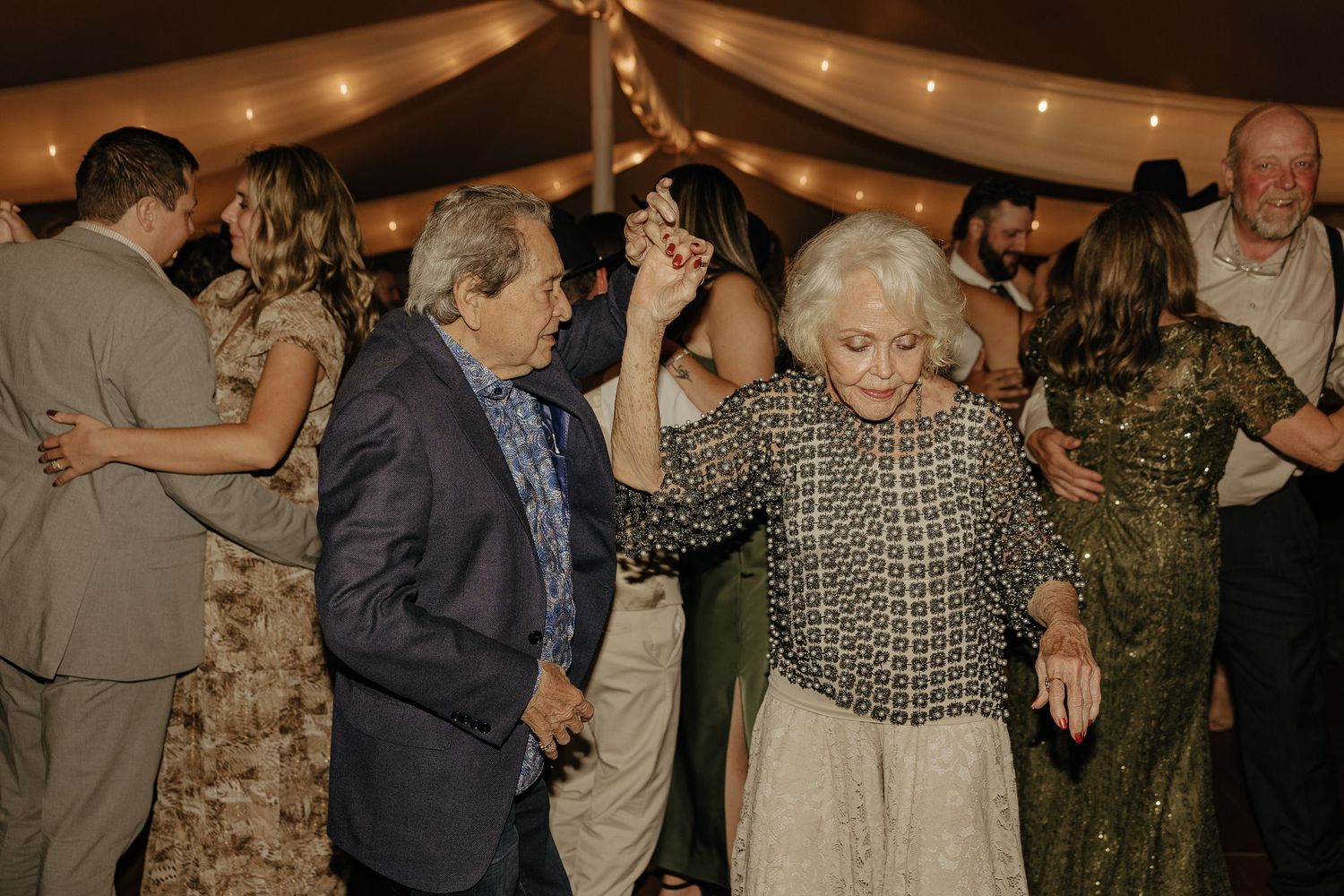 Wedding guests dance and celebrate together under a tent at an evening reception.
