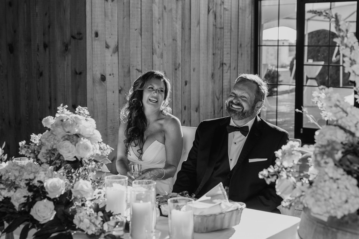 A rustic barn wedding reception setup with white floral centerpieces and wooden tables decorated with candles and greenery.