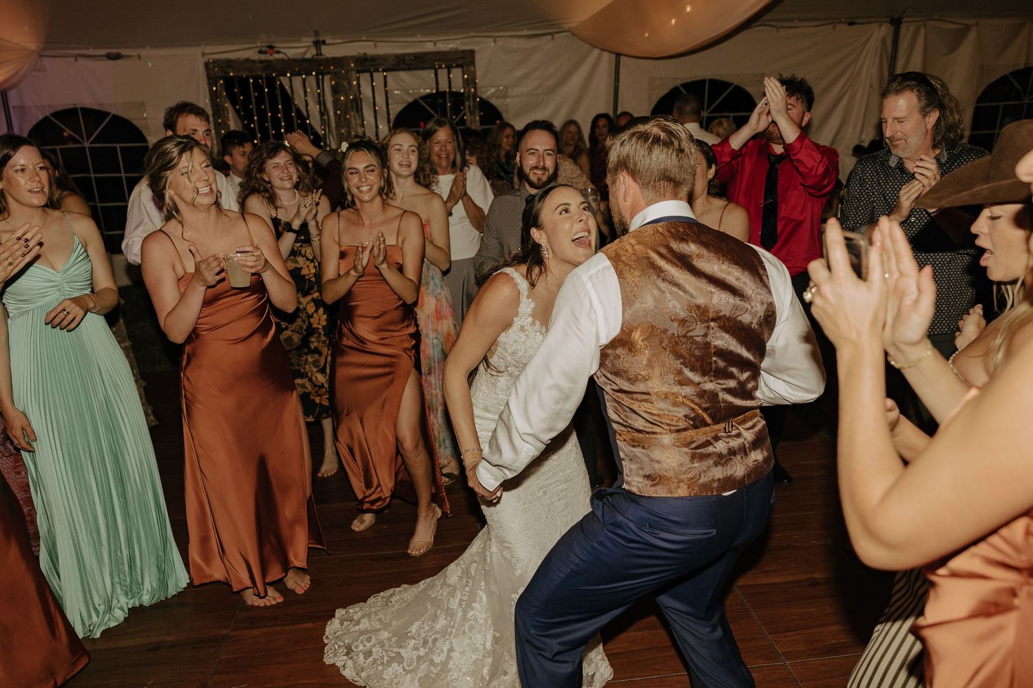Large group of wedding guests dancing together on a wooden dance floor at an evening reception.
