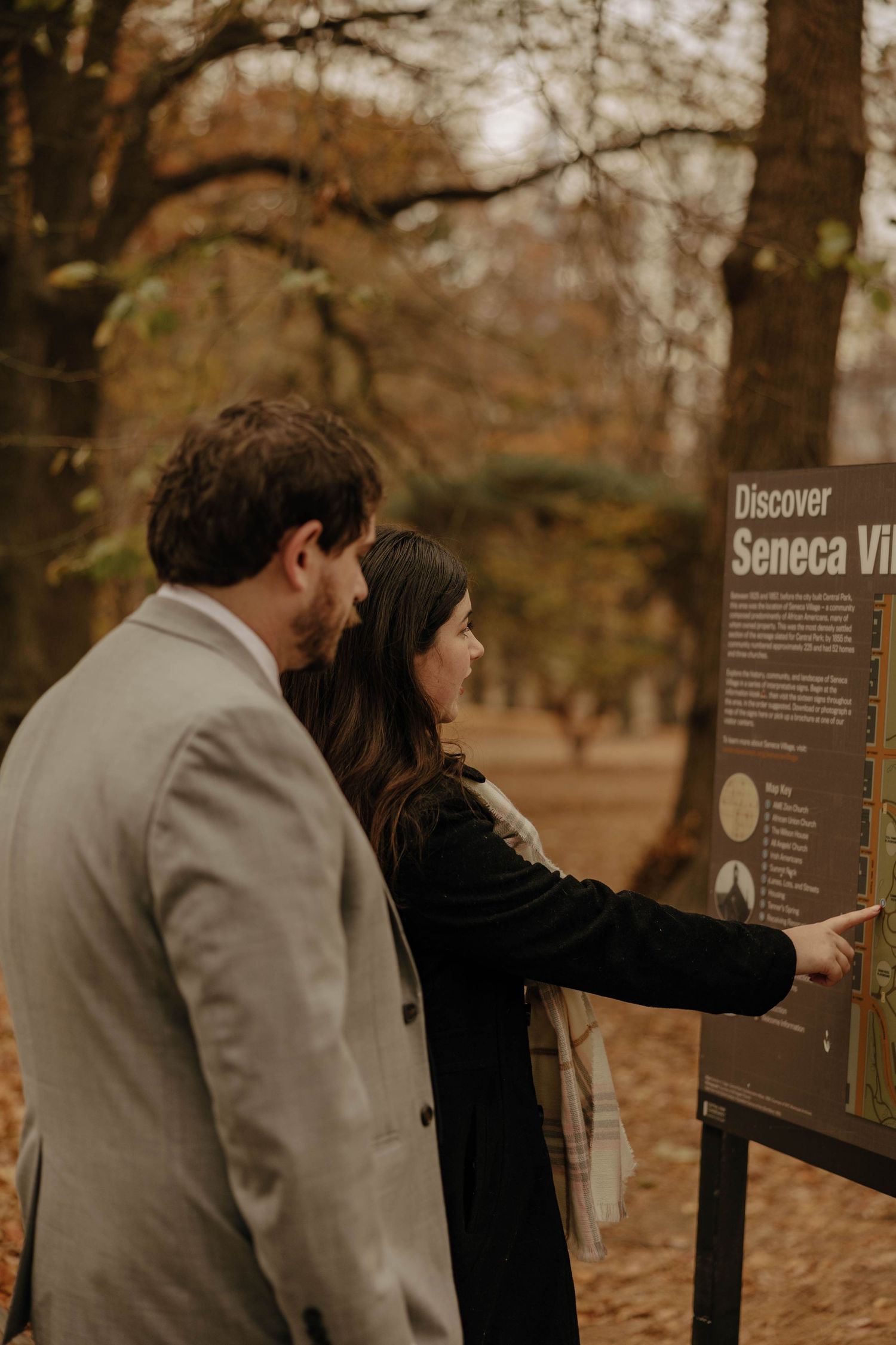 A couple reads informational signs along a park trail during an autumn day.