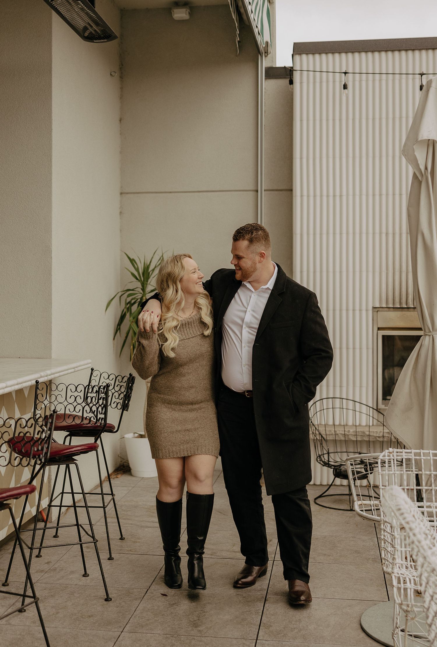 A couple shares a playful moment in a minimalist indoor space with white chairs and modern decor.