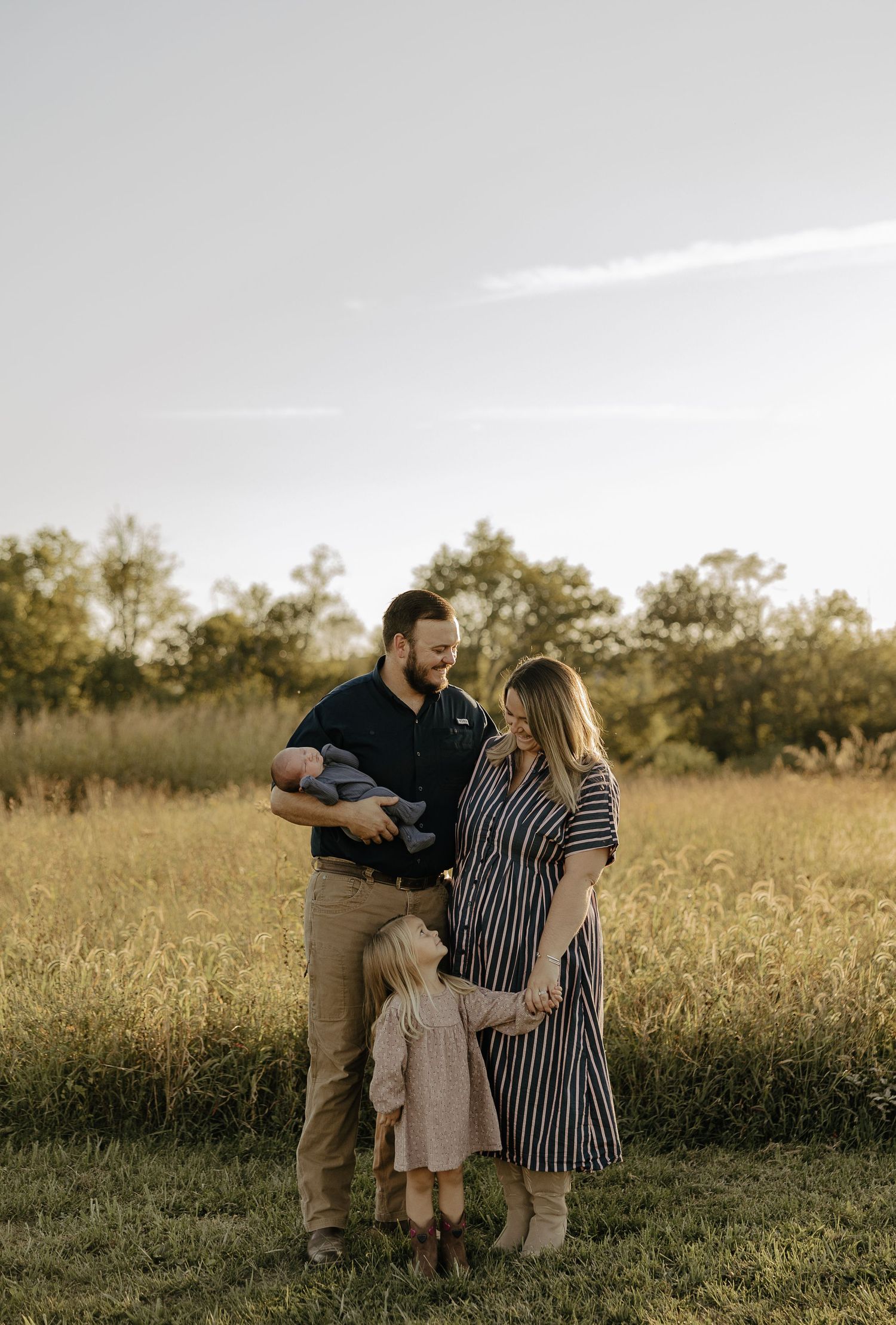 Family of three embracing and laughing together in a golden field.