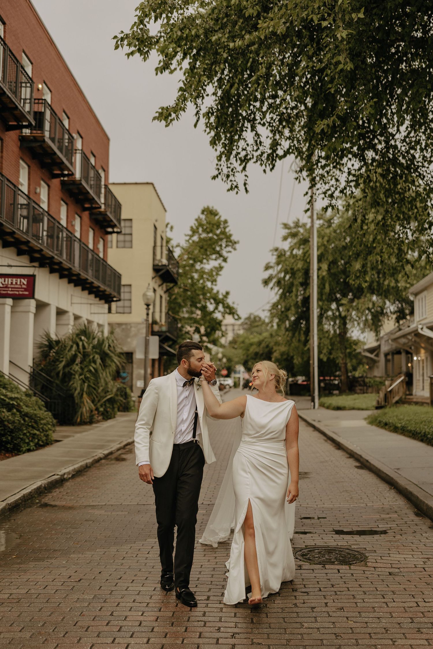 A wedding couple walks together on a charming brick-paved street lined with historic buildings.