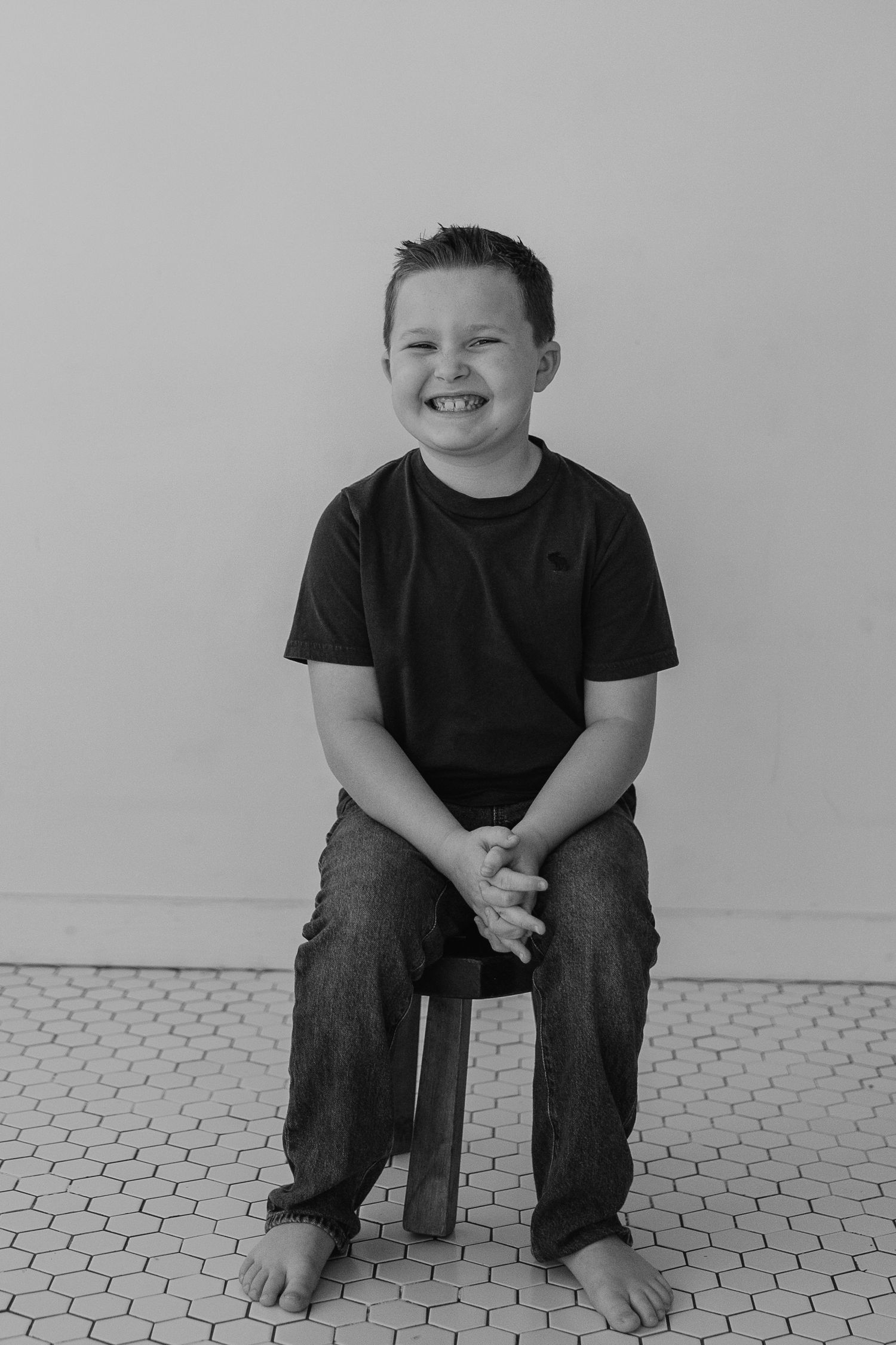 Black and white portrait of child sitting on wooden stool showing genuine happy expression.