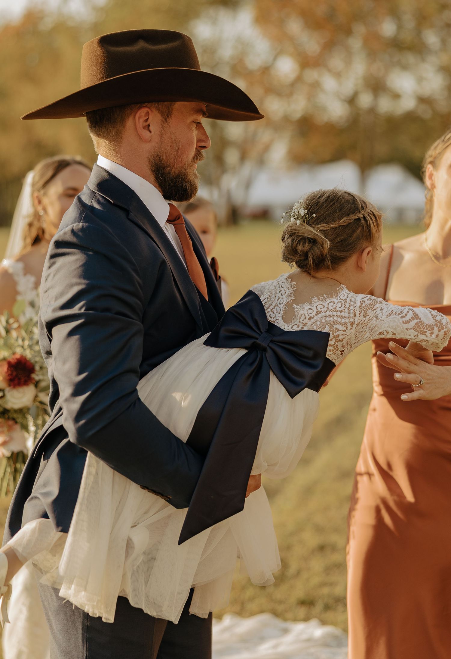 Wedding party members in navy suits and earth-toned dresses with a large decorative bow accent.
