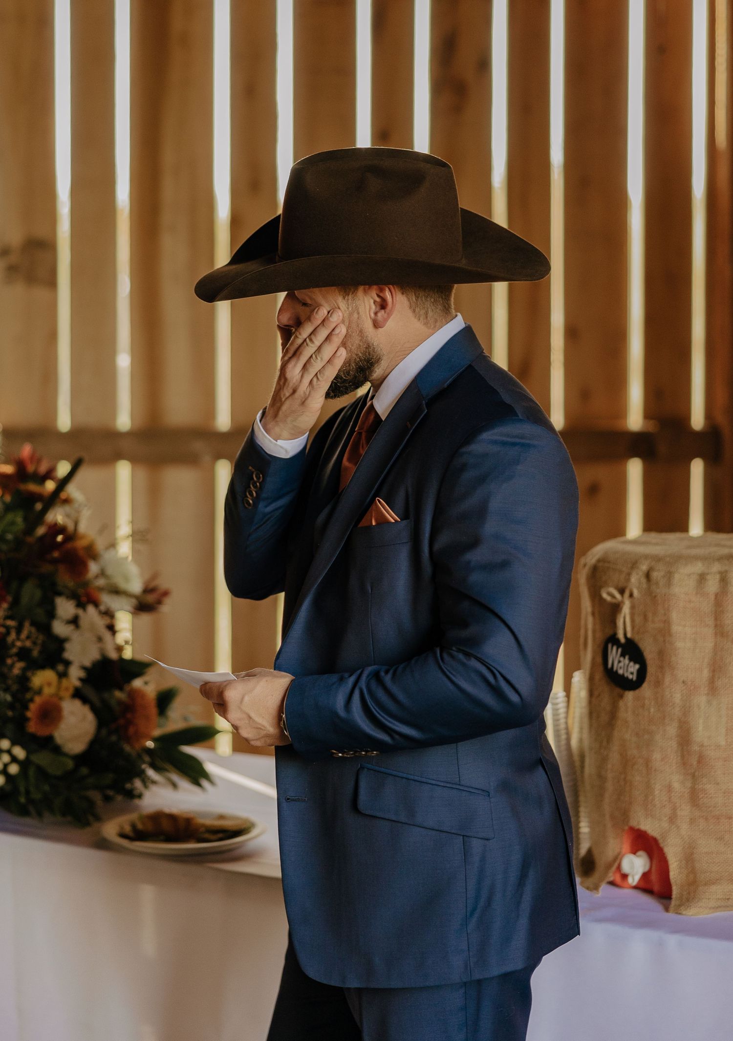Person in navy suit and cowboy hat standing in rustic indoor venue.