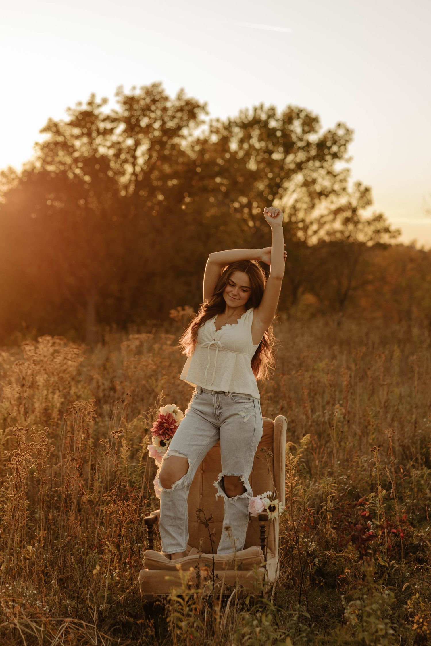 A dreamy golden hour portrait session in a rustic field with a vintage chair and warm sunset lighting.