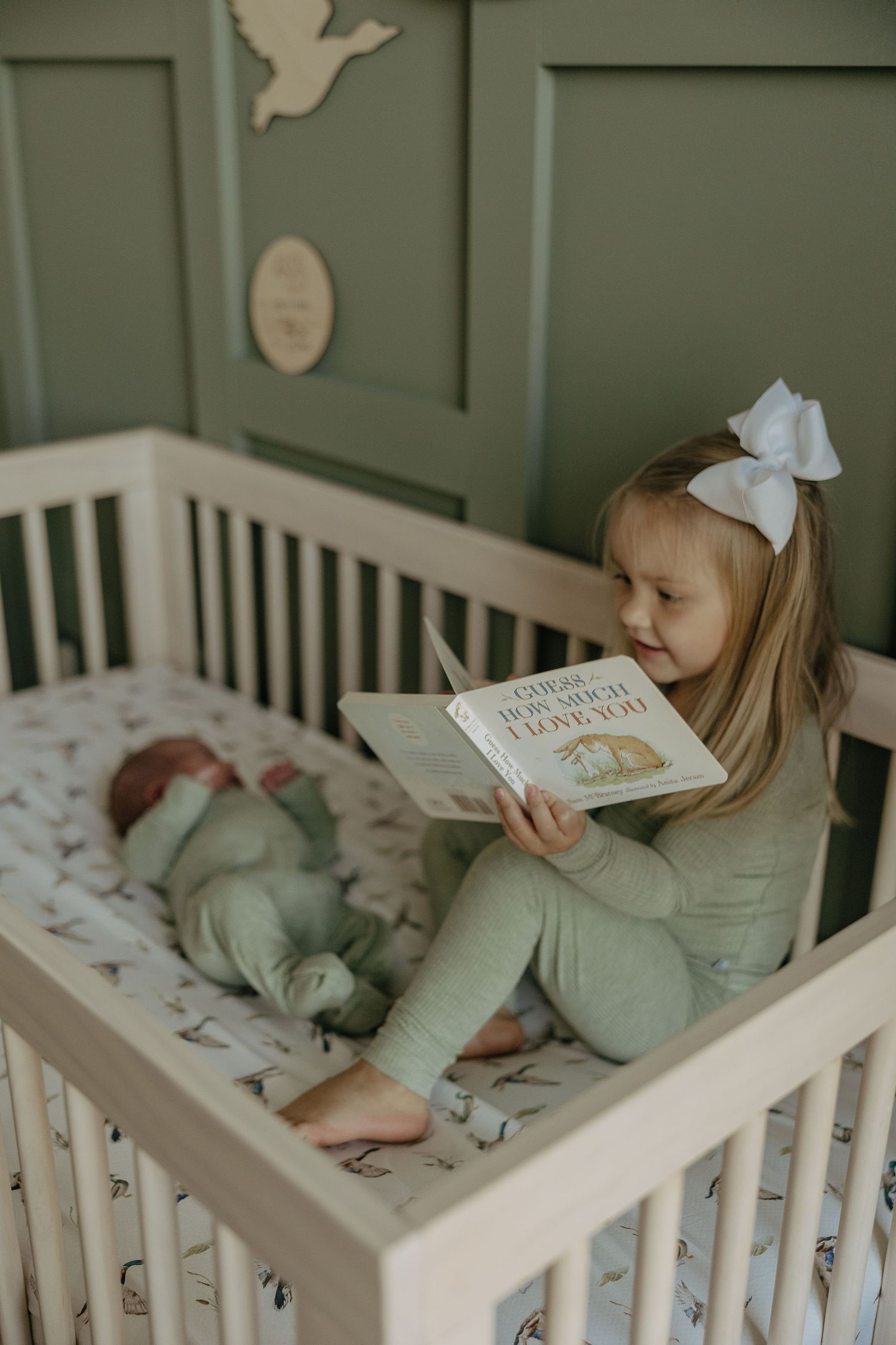 Child reading a book while relaxing in a white crib with patterned bedding.