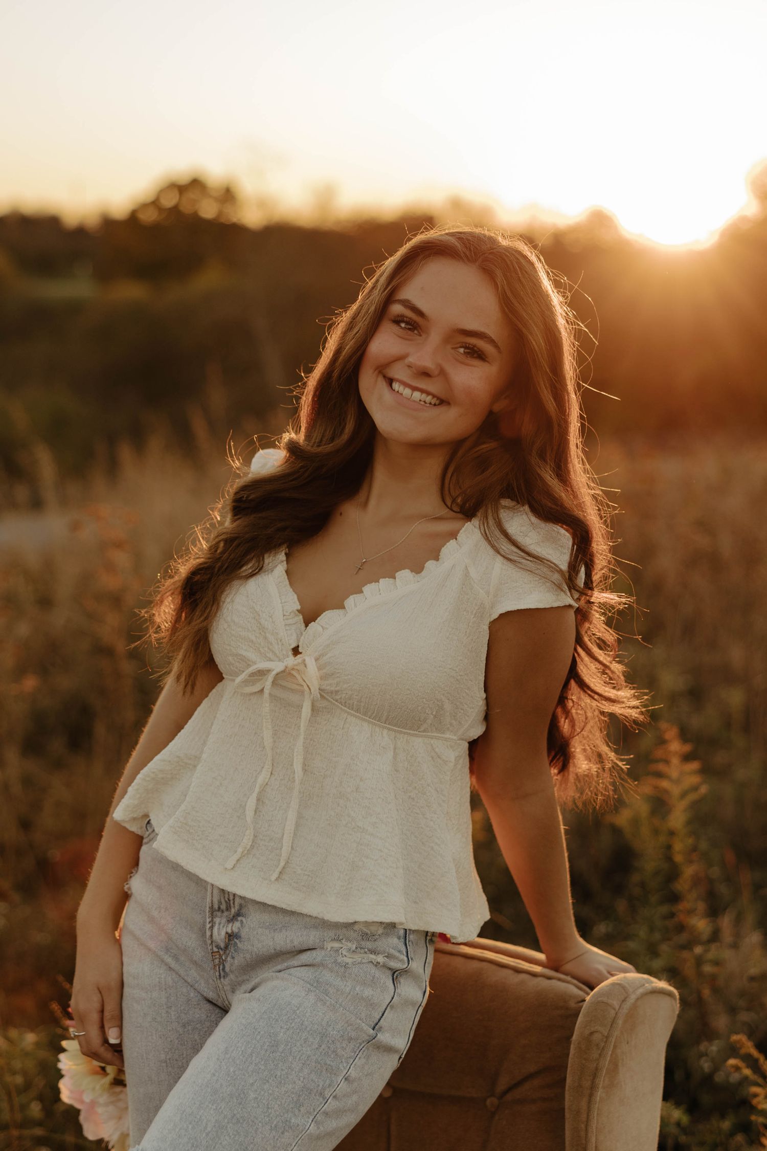 Joyful summer portrait session in a field with golden sunlight and white lace top.