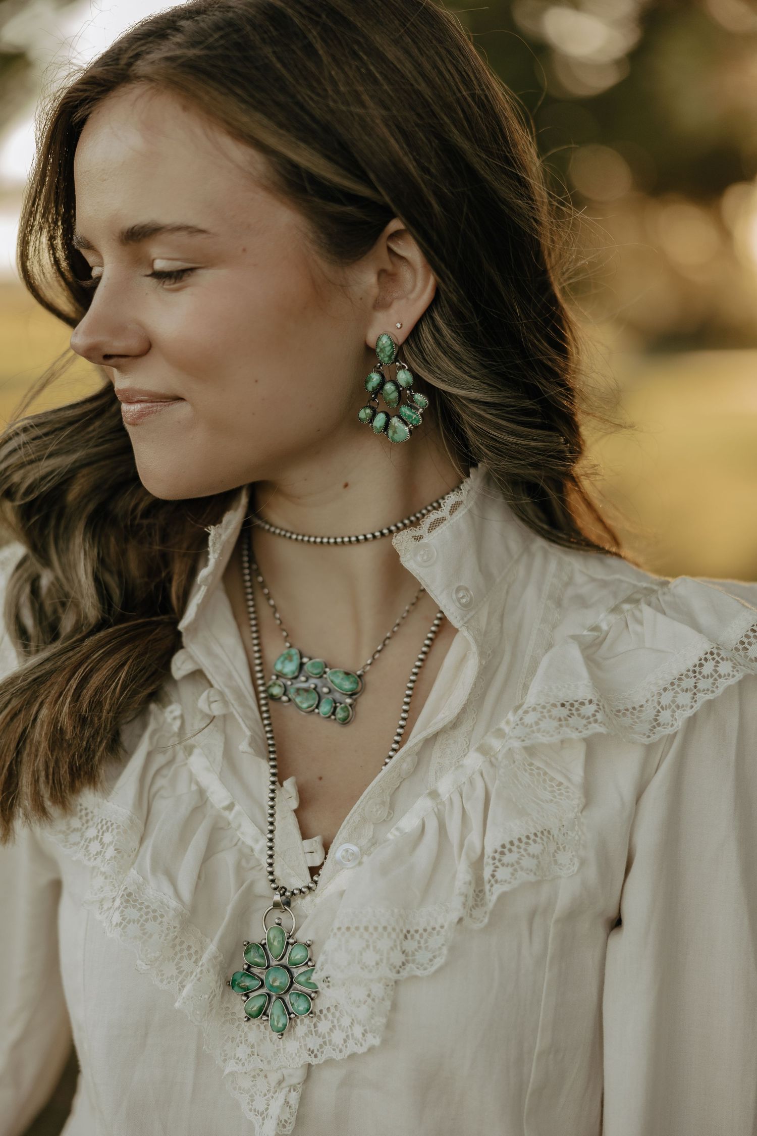 Turquoise statement jewelry set featuring earrings and layered necklaces paired with a white lace blouse in golden light.
