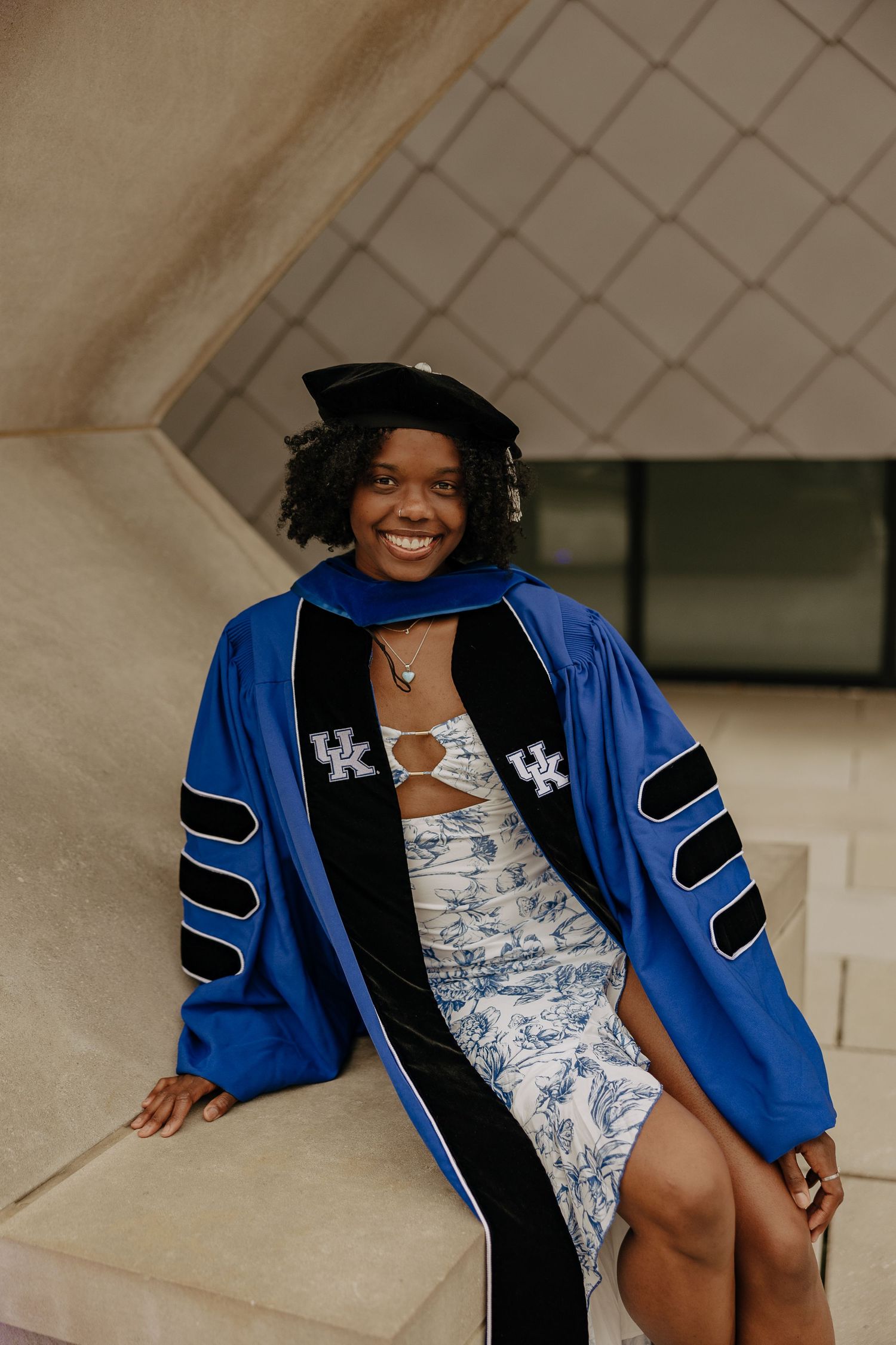 Academic graduation portraits featuring blue and black doctoral regalia against stone wall.