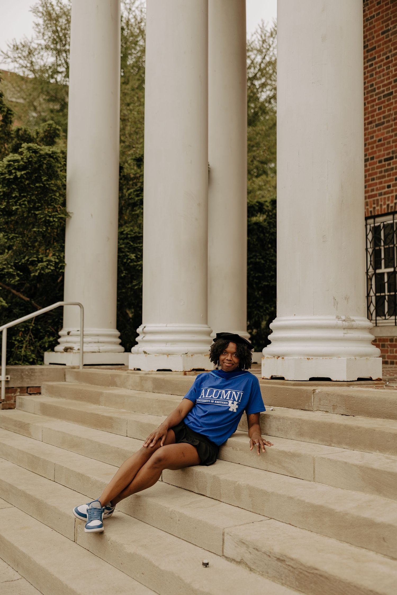 Graduate reclines dramatically on white stone steps between classical columns.