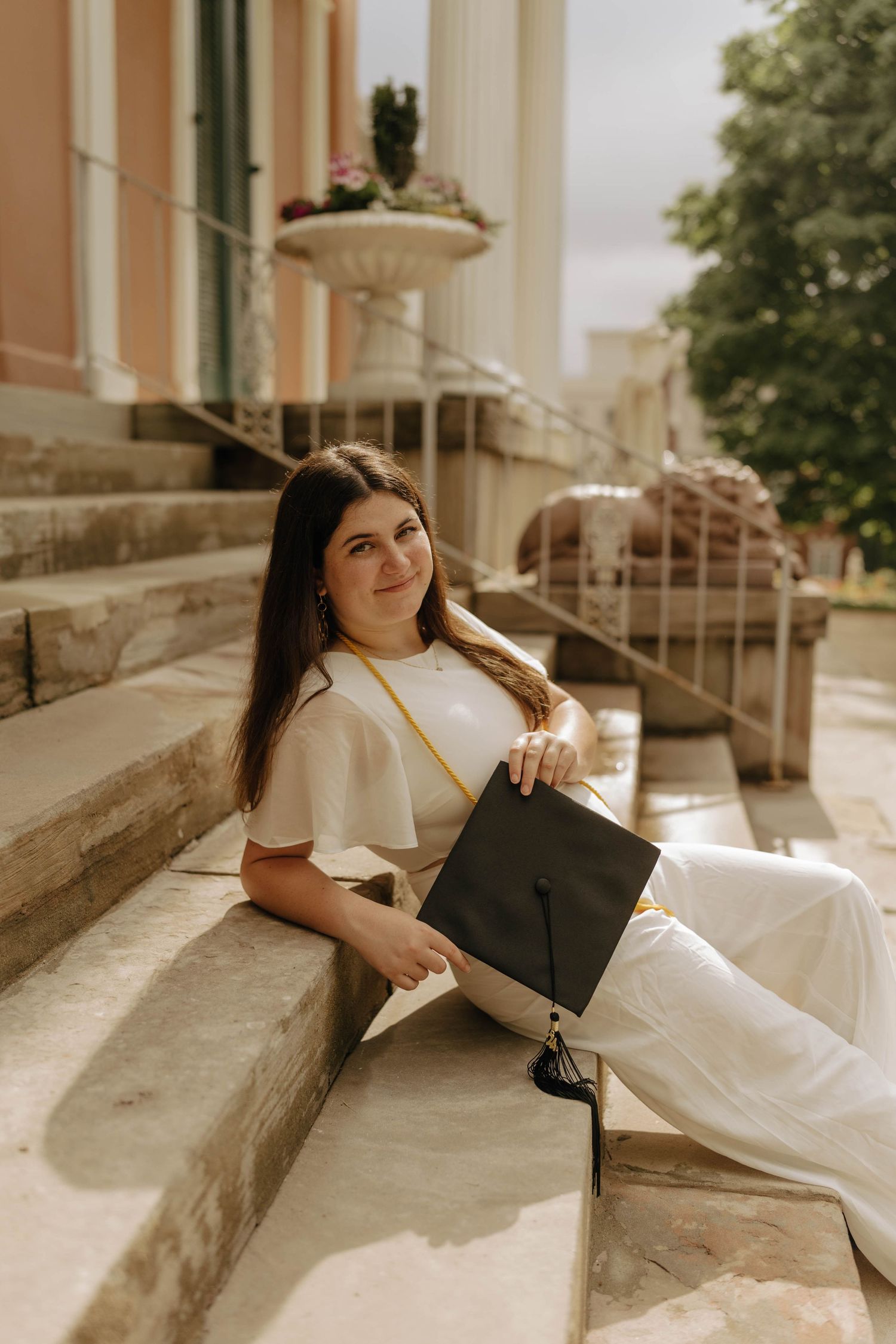 A graduate in cap and gown reclines on stone steps during a photo session.