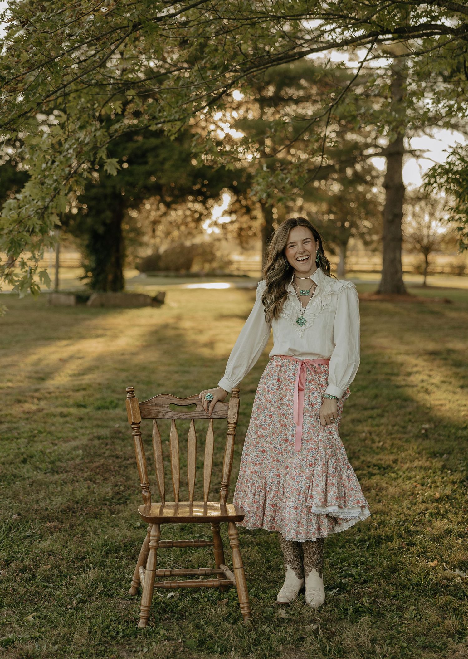 A floral dress and white blouse outfit photographed in a sunlit outdoor setting with vintage wooden chairs.