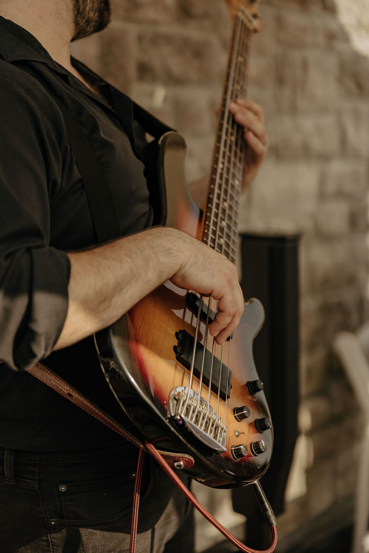 Close-up of musician playing bass guitar against stone wall background.