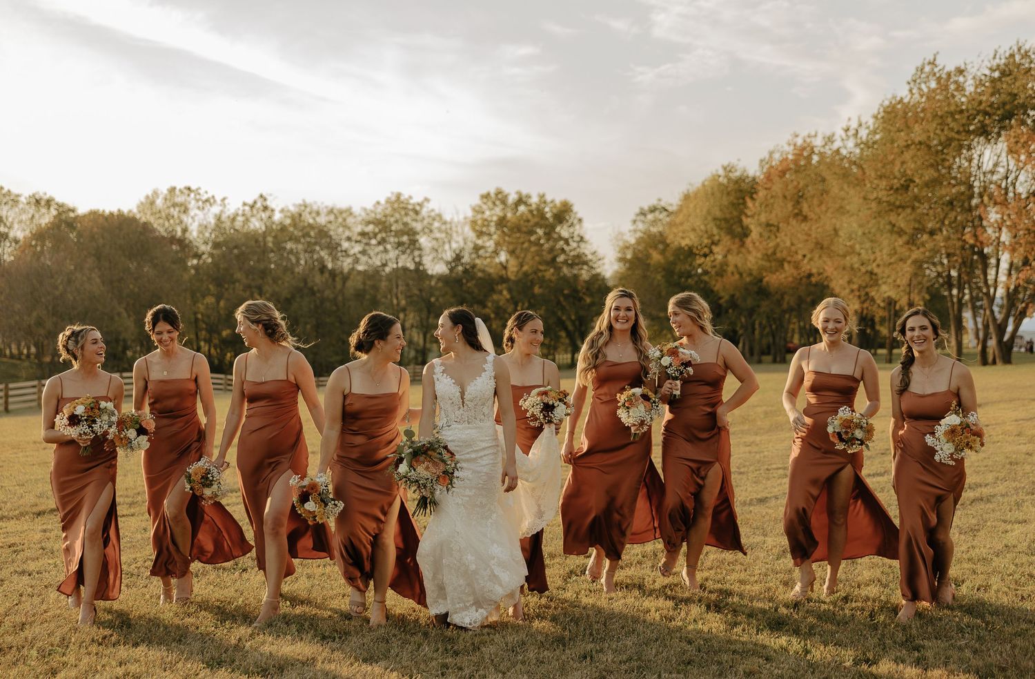 Wedding party in burgundy dresses poses in a line at sunset in a field.