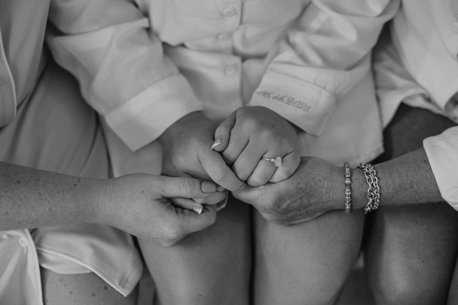 Close-up view of bridesmaids' hands clasped together while wearing matching white robes.