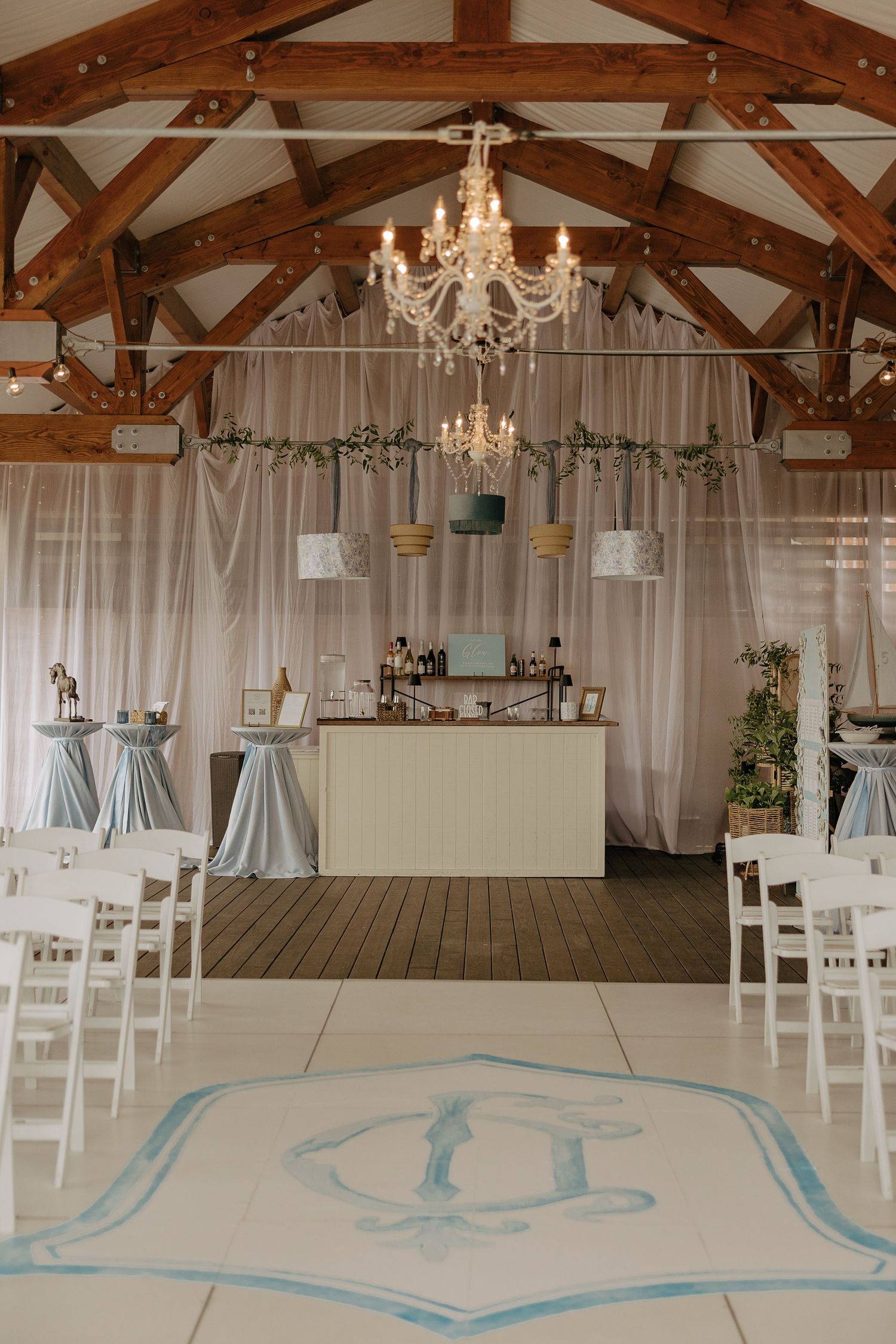 Elegant wedding venue interior with exposed wooden beams, crystal chandeliers, and light blue floor designs.