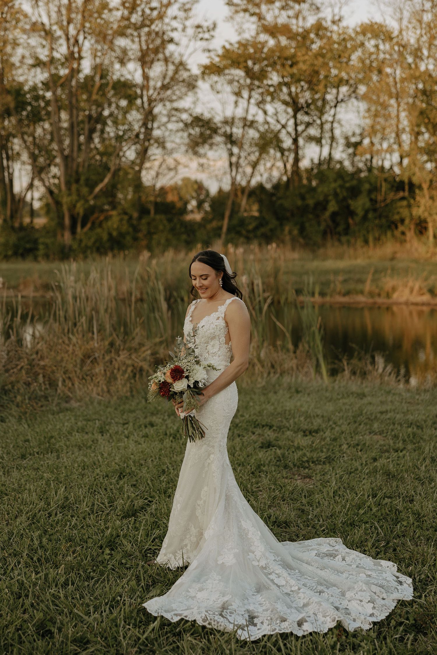 Elegant lace wedding dress with long train photographed in a natural outdoor setting at sunset.