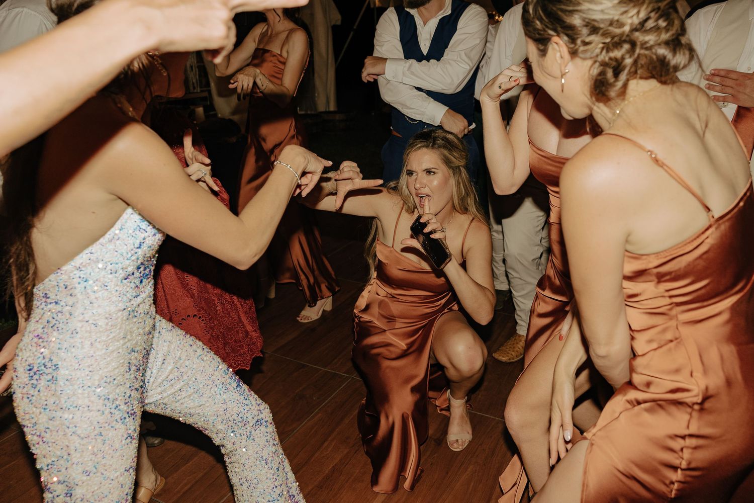 Wedding reception guests dancing and celebrating on a dimly lit dance floor with warm lighting.