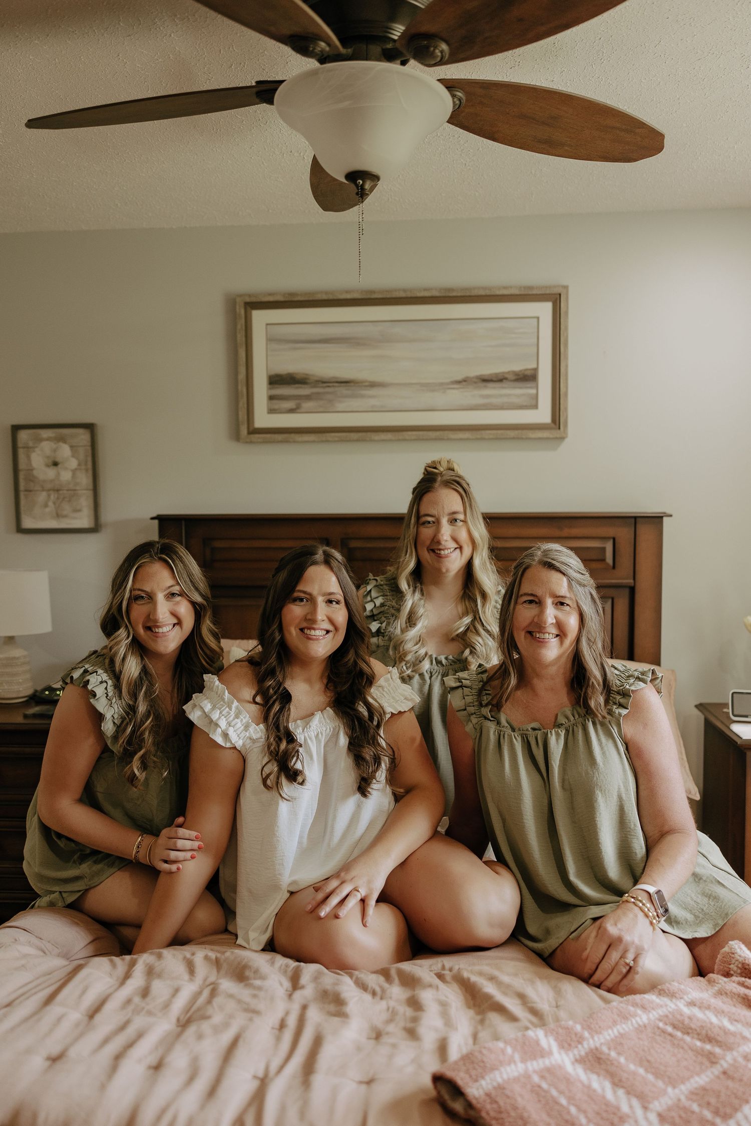 Group of friends in sage green and white outfits lounging together on a pink bed during a casual photoshoot.