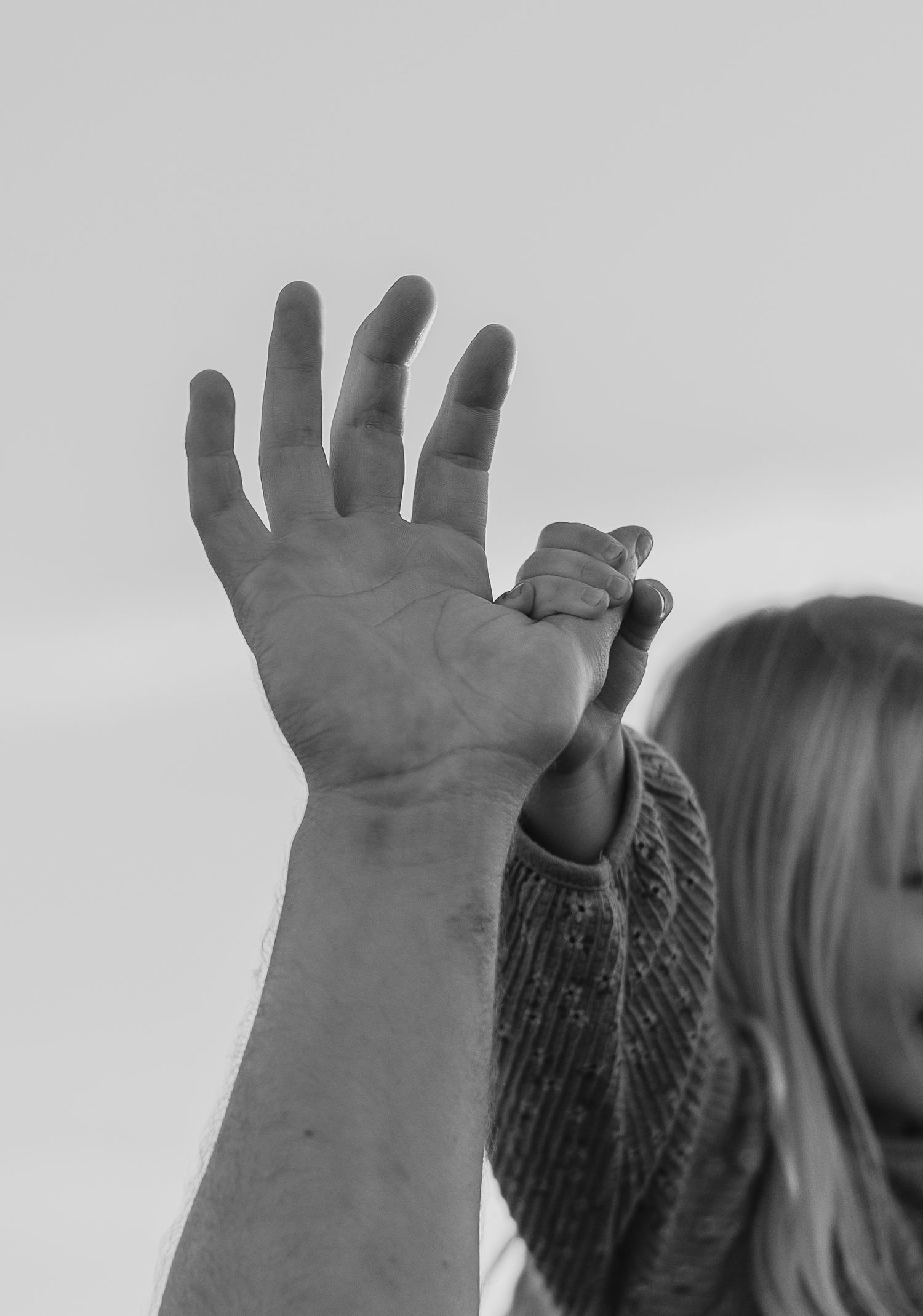 Silhouetted hands reach up against a bright sky in a celebratory gesture.